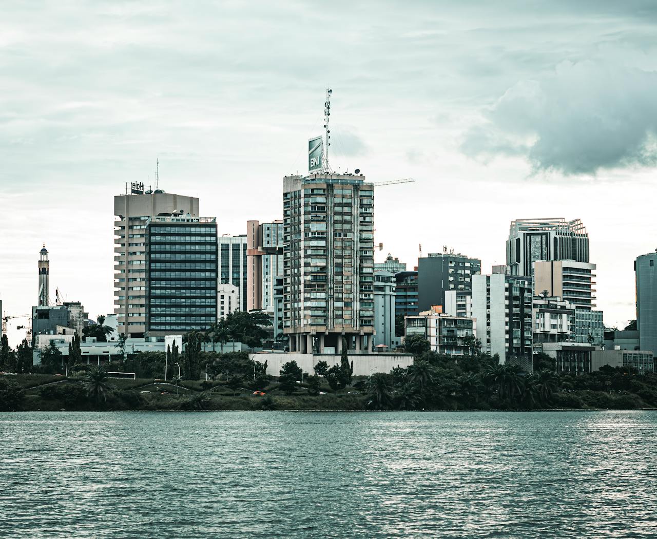 hero-img-02 Contemporary cityscape of Abidjan featuring high-rise buildings by the waterfront under overcast skies.