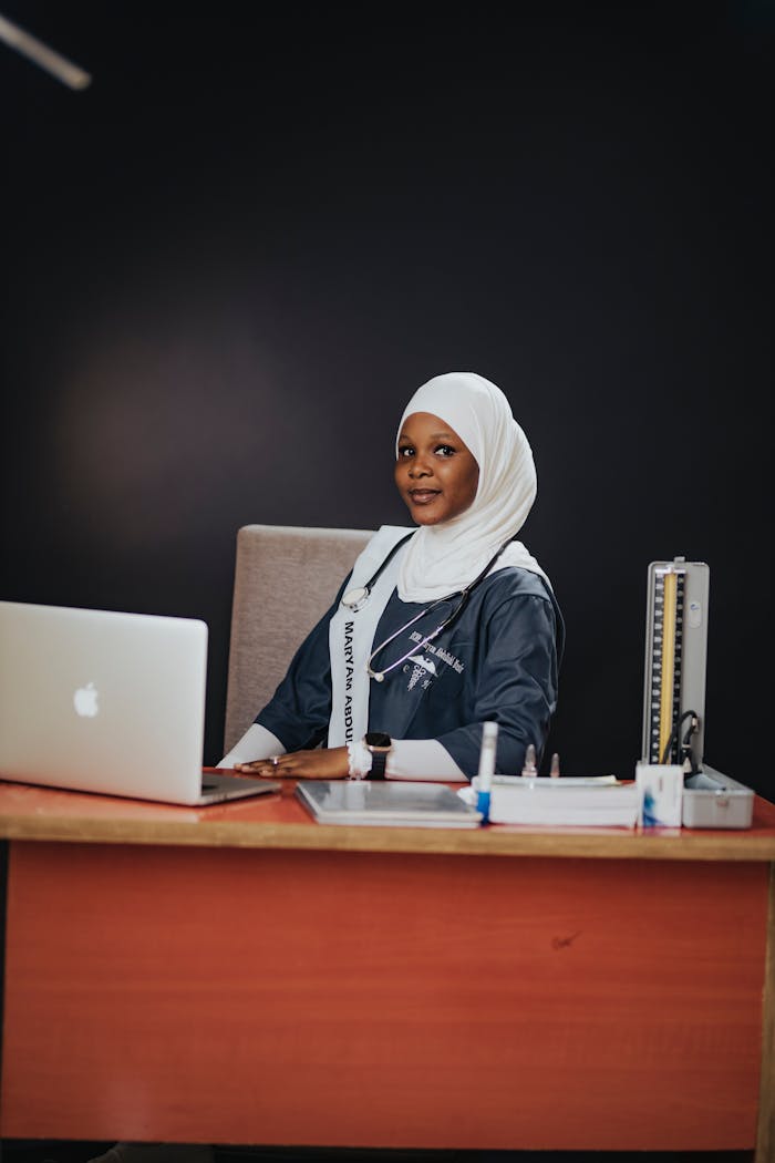 why-choose-us A smiling graduate in a cap and gown sitting at a desk with a laptop, symbolizing success.